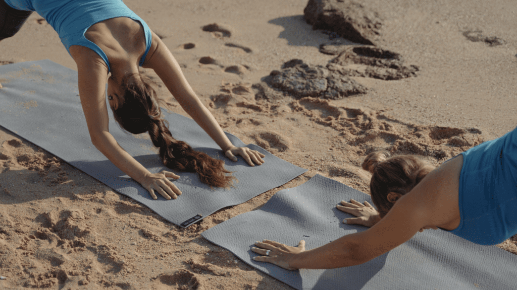 Two women do yoga on a sandy beach